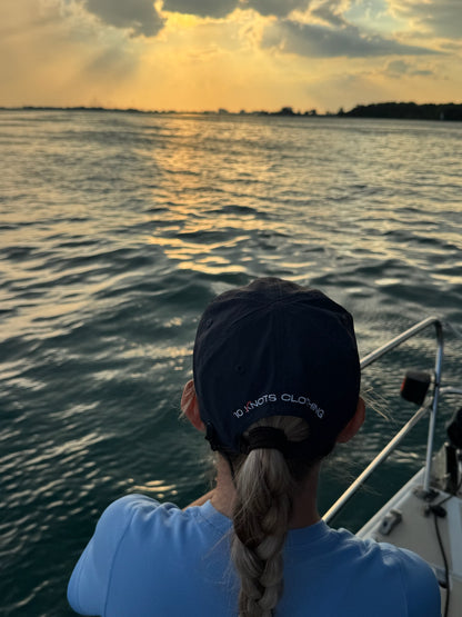 Person on saill boat wearing 10 Knots Great Lakes hat looking at the sunset over water